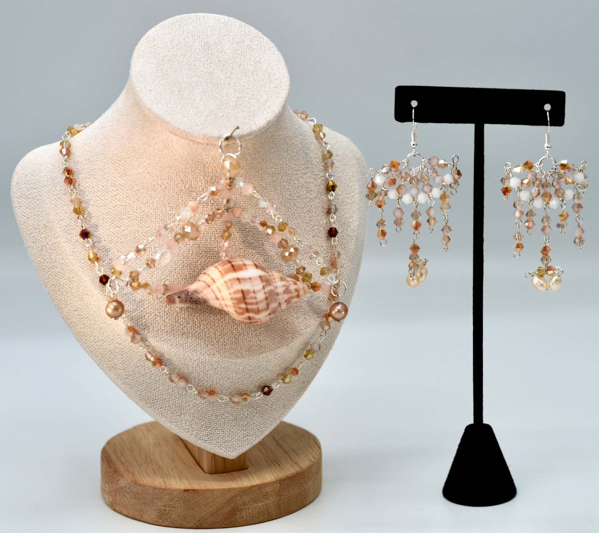 Beaded necklace and earrings on a mannequin bust and black stand against a light gray background